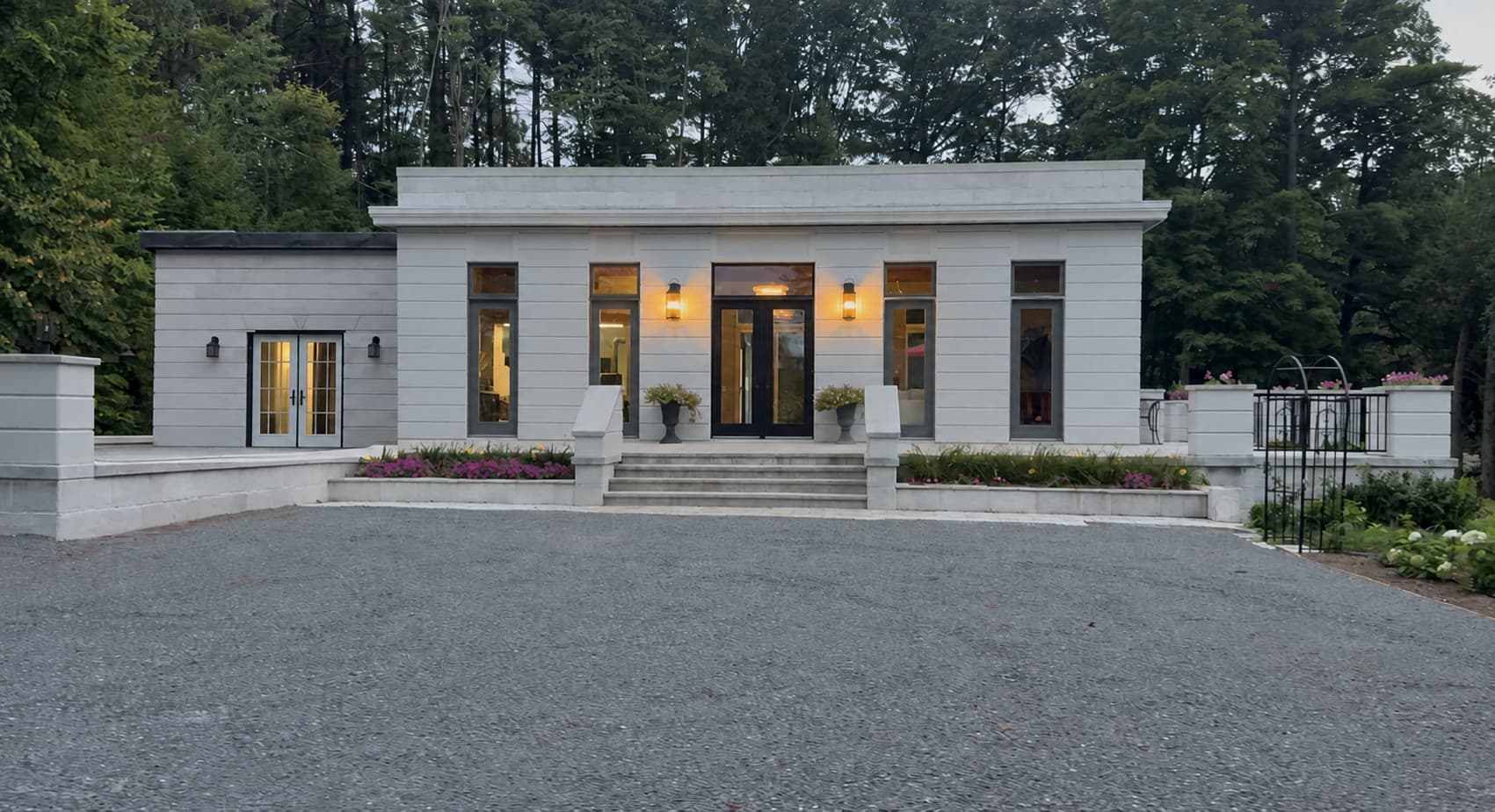 Façade avant de la maison modèle Thermobloc au crépuscule, murs au fini pierre et entrée éclairée